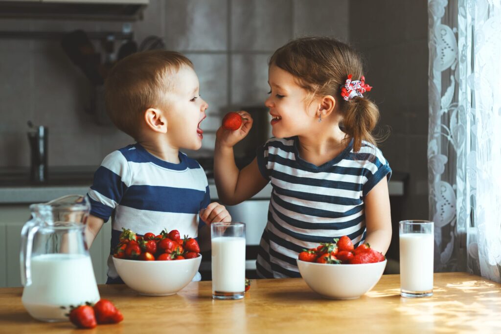 girl feeding strawberries to boy in a striped shirt