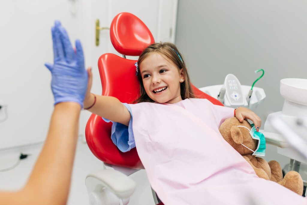 girl in red dental chair giving a high five
