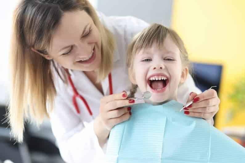 Pediatric dentist examining smiling child’s teeth