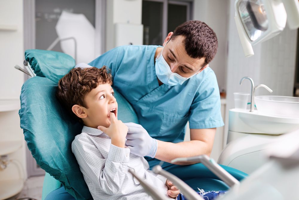 child points to mouth while dentist examines teeth