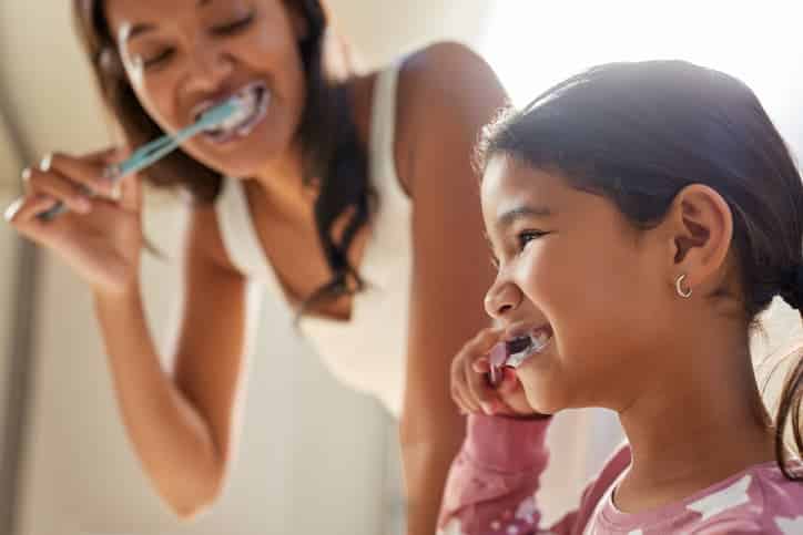 Mother and daughter brushing their teeth together at home