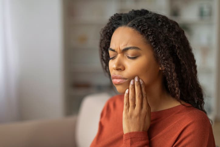 Woman holding her cheek while experiencing tooth pain at home
