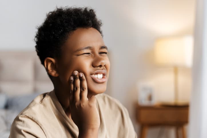 Young boy experiencing tooth pain while holding his cheek at home