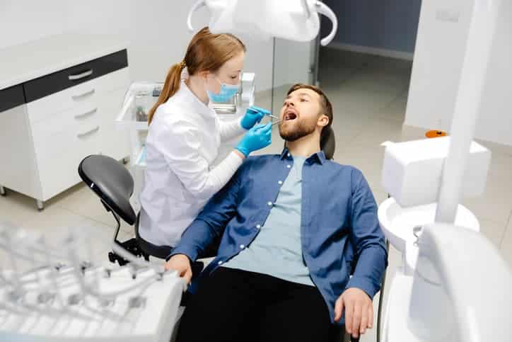 Dentist performing an oral examination on a male patient in a dental clinic