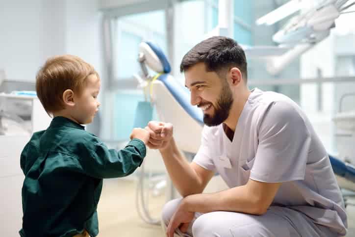 Pediatric dentist greeting a young child with a fist bump in a dental clinic