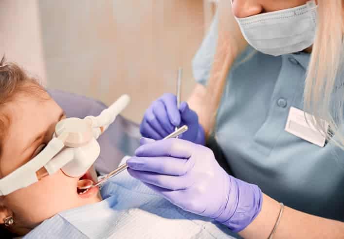 Dentist performing a child dental examination with protective eyewear and tools