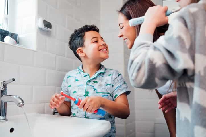 Mother and children brushing their teeth together in a family bathroom