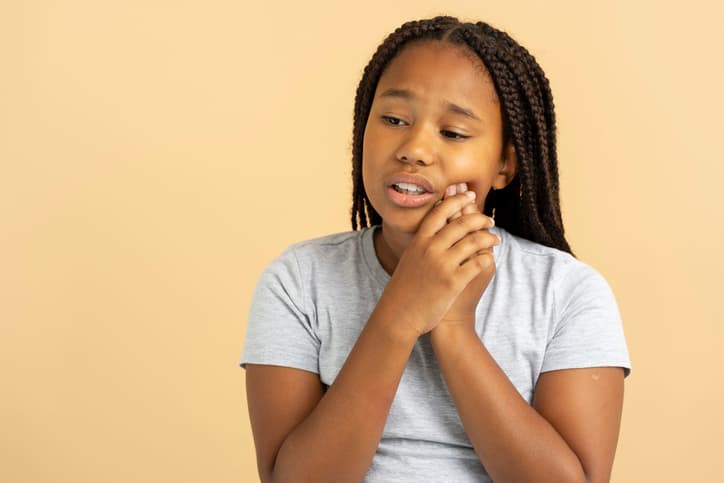 Young girl holding her cheek while experiencing tooth pain