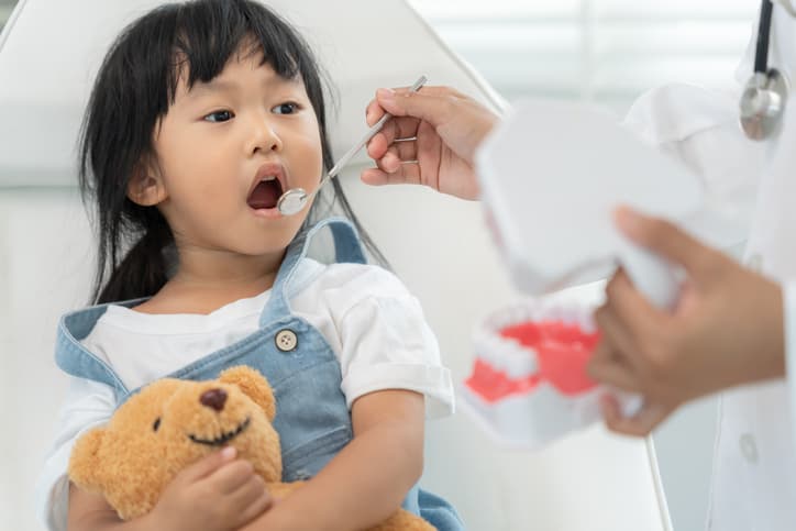 Young girl holding a teddy bear during a pediatric dental examination