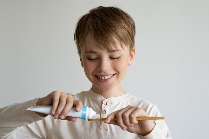Young boy applying toothpaste to a toothbrush before brushing his teeth