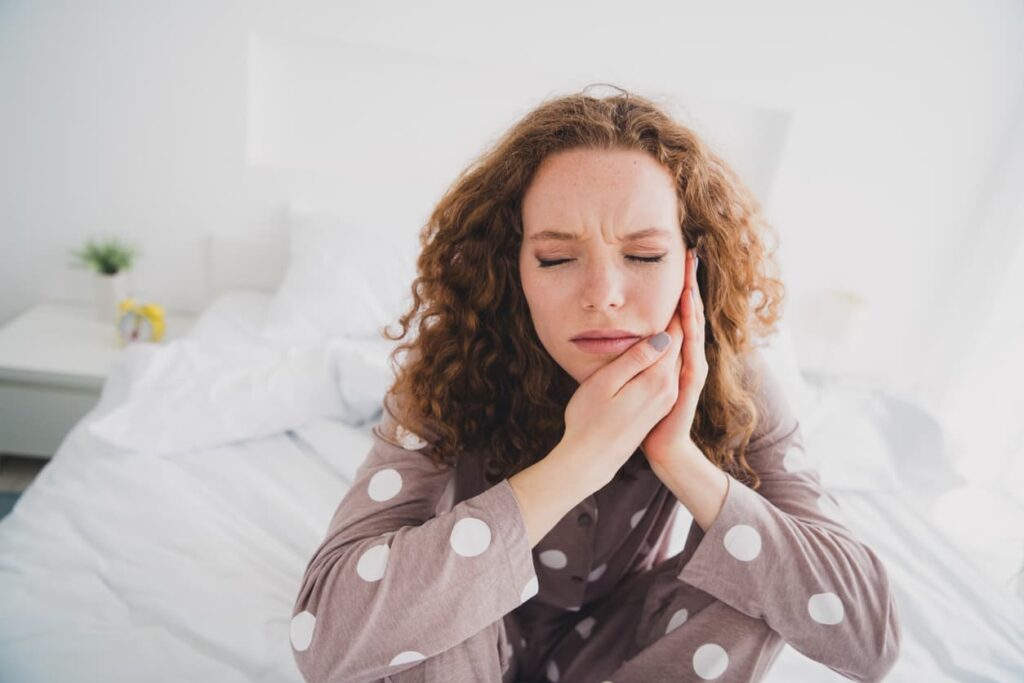 Woman holding her jaw in pain while sitting in bed with a toothache