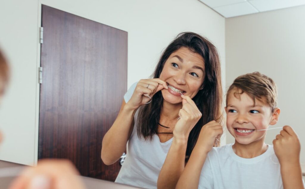 dental emergencies (1) Mother and child flossing their teeth together in front of a bathroom mirror