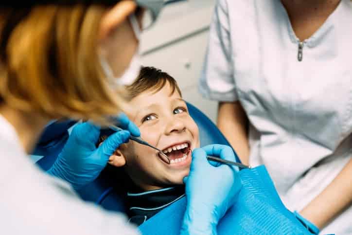 Young boy smiling during a dental exam while a dentist checks his teeth