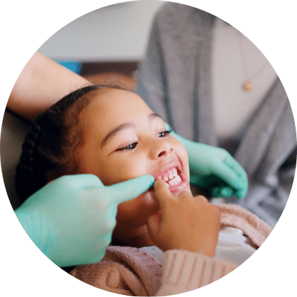 Child smiling and pointing at her teeth in a mirror during a dental visit