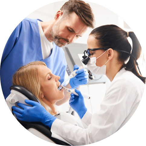 Dentist examining a patient’s teeth while an assistant supports during treatment