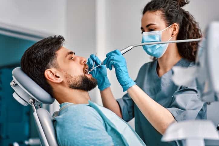 Dentist performing a dental exam on a male patient using suction and dental tools