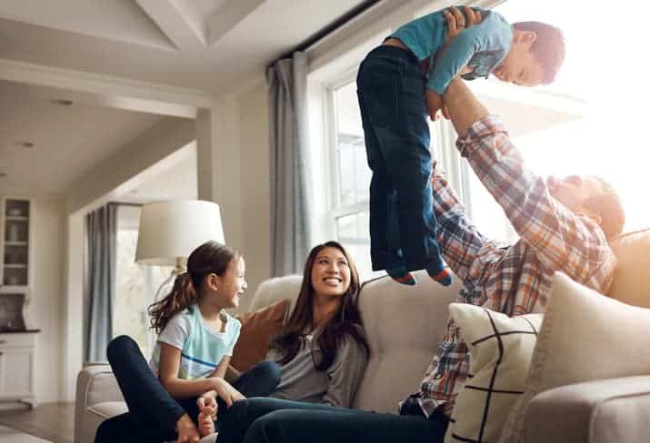 Father lifting his child in the air while family sits together on a couch at home