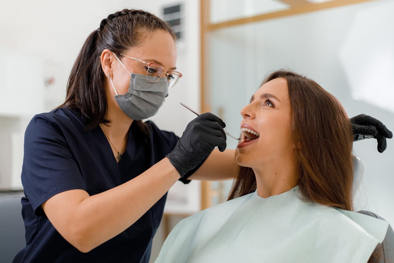Female dentist performing an oral exam on a patient using dental tools and mirror