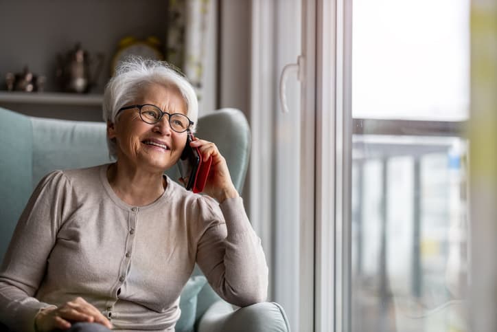 Older woman smiling while talking on the phone by a window at home