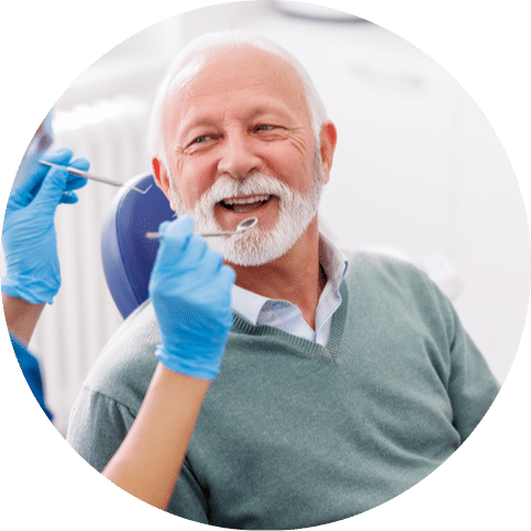 Older man smiling during a dental exam while a hygienist checks his teeth