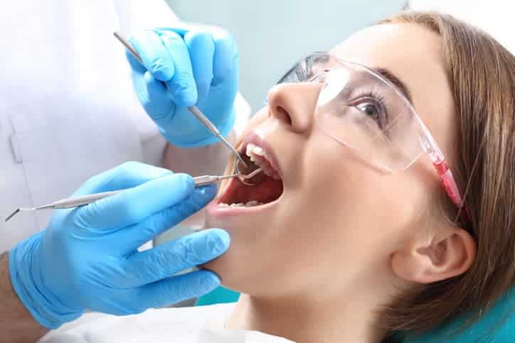 Patient wearing protective glasses during a dental exam as tools are used to check teeth