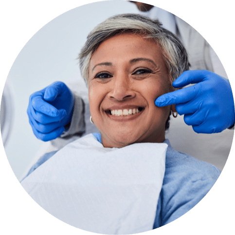 Woman smiling and looking in a mirror while a dentist examines her teeth