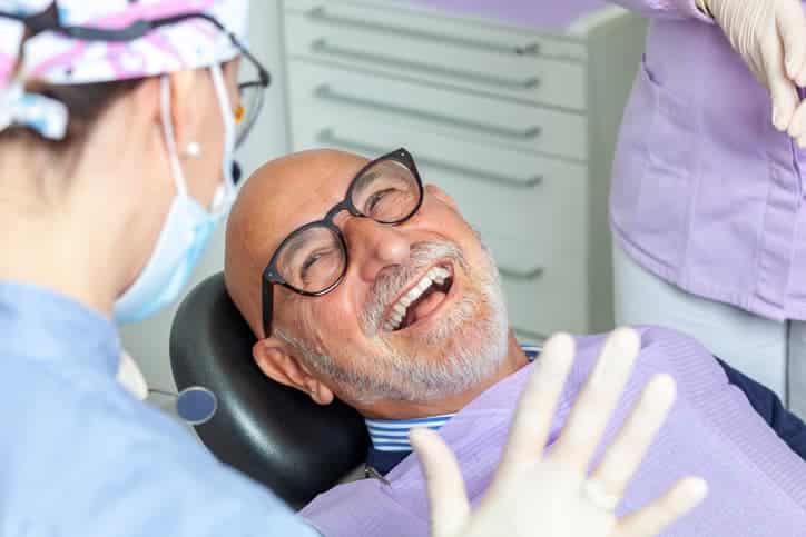 Senior man smiling in dental chair while dentist and assistant prepare for treatment