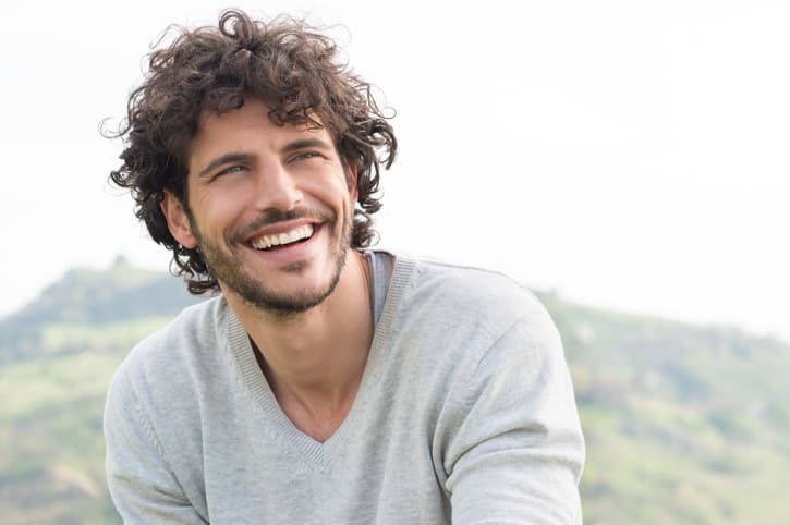 Man smiling outdoors with a scenic landscape in the background