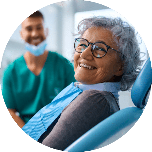 Older woman smiling in a dental chair with a dentist in the background