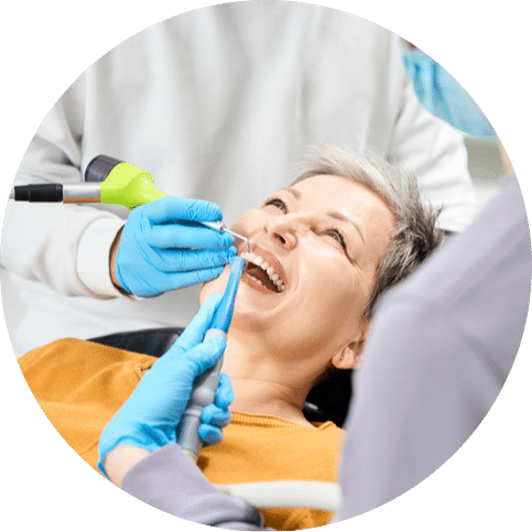 Woman smiling during a dental procedure while a dentist and assistant work on her teeth