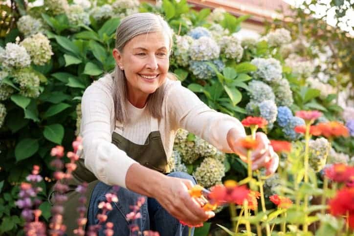 Woman pruning flowers in a garden surrounded by blooming plants
