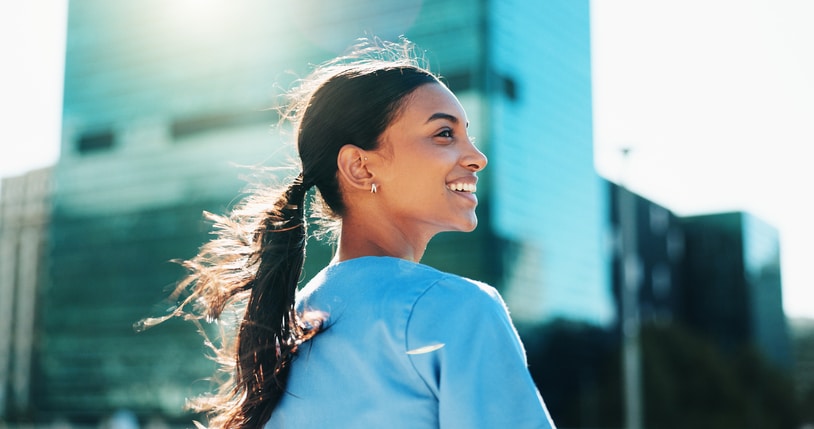 Woman smiling outdoors with city buildings in the background