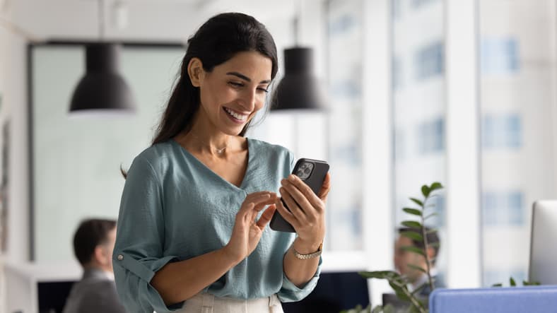 Woman smiling while using smartphone in modern office environment