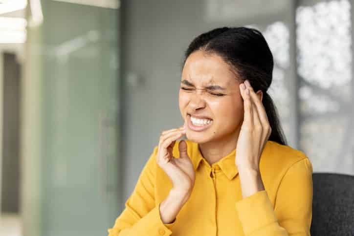 Person holding their jaw and temple while experiencing severe tooth pain, illustrating the discomfort of a toothache, dental infection, or other oral health emergency requiring prompt dental care.