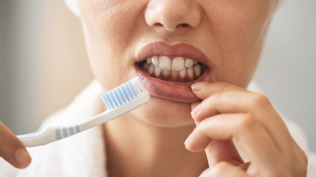 Person holding a toothbrush while checking plaque buildup along the gums