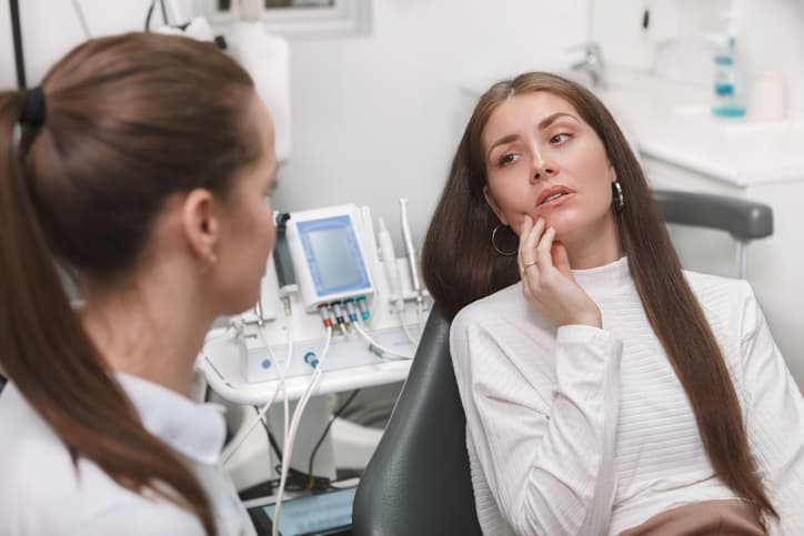Woman experiencing tooth or jaw pain while speaking with a dentist during an appointment in a dental clinic