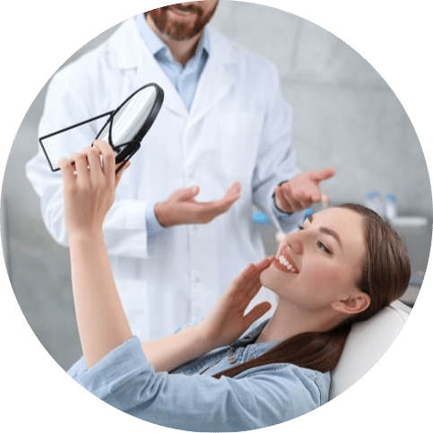Patient smiling and looking at her teeth in a mirror while discussing the results of dental crown treatment with her dentist